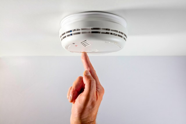 An image of a finger pressing a white smoke alarm