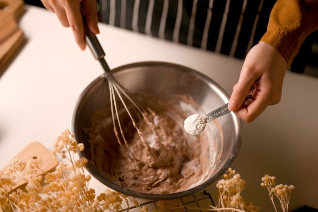 An image of a person holding holding a teaspoon of baking soda over a bowl of dough