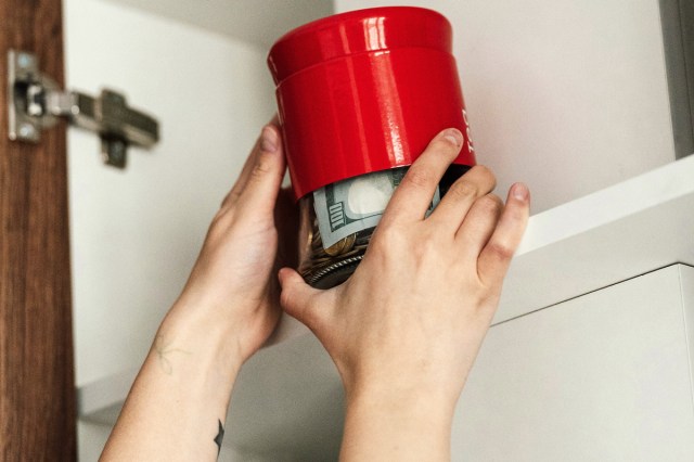 An image of a woman holding a red jar with money