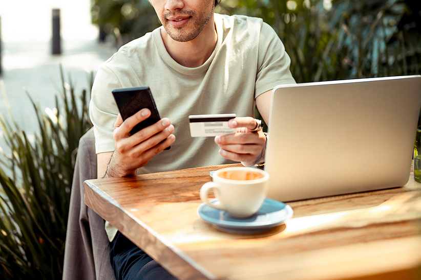 An image of a man on a laptop and holding his phone and credit card