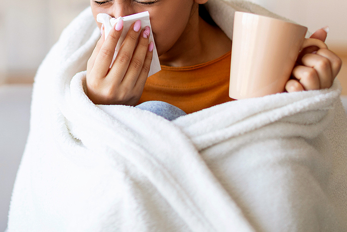 An image of a woman holding coffee mug and blowing her nose