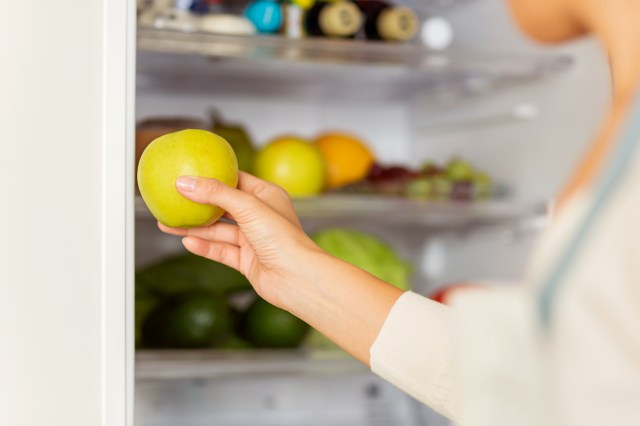 An image of a woman taking a green apple out of the fridge