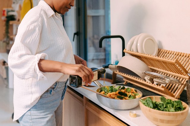 An image of a woman dressing a salad with olive oil