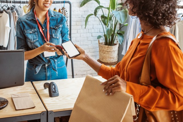 An image of a woman tapping her phone on a credit card machine at a store