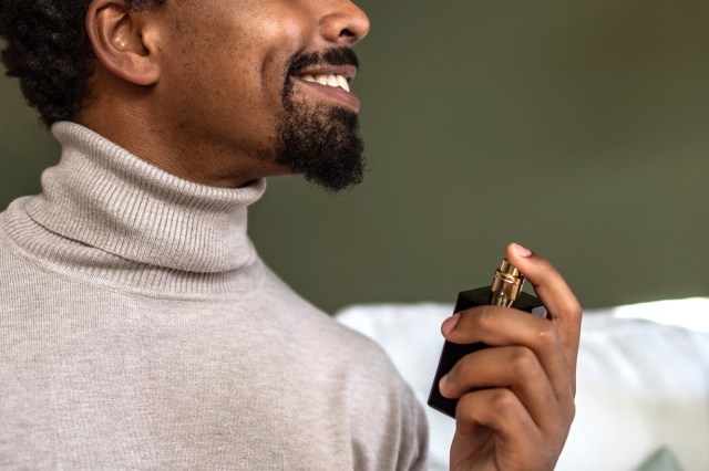 A man smiles while he sprays perfume on himself