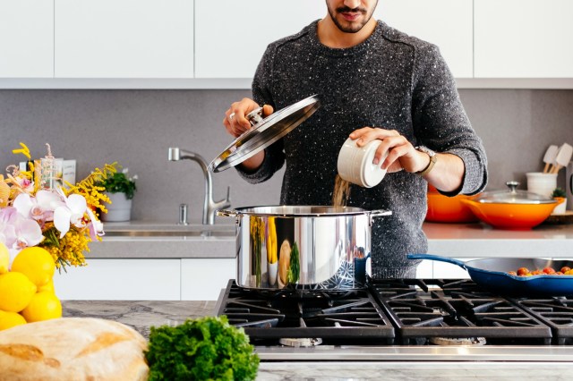 An image of a man pouring something into a pot on the stove