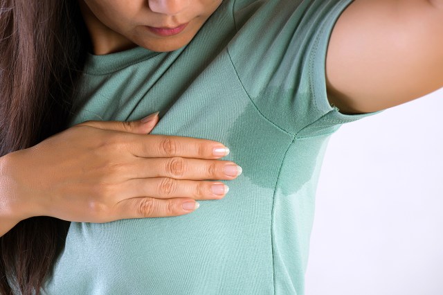 An image of a woman looking at an armpit sweat stain on her shirt