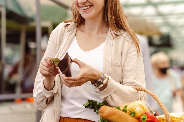 Woman shopping with basket of fruit and vegetables while looking at wallet