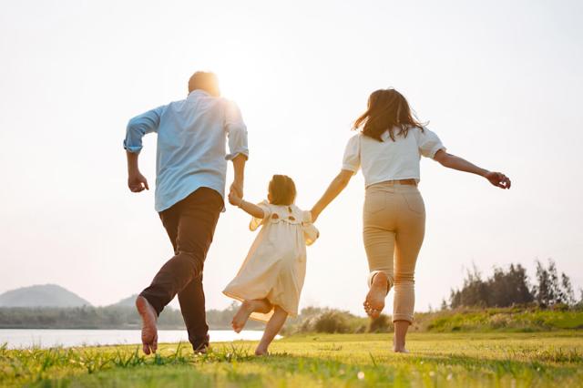 Parents holding hands with their child and running through a field barefoot