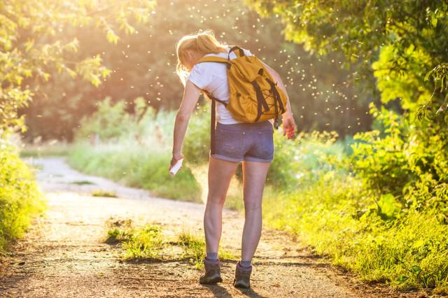 Woman with a backpack spraying bug spray to keep bugs away