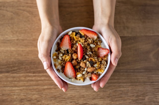 Someone holding a bowl of yogurt parfait with granola, strawberries and rice krispies in it