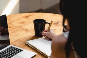 Woman writing in notebook with a cup of coffee and computer