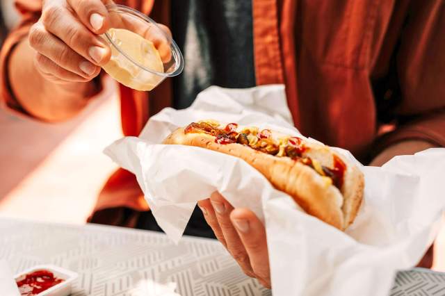 Person putting peanut butter on a hot dog that has ketchup and mustard on it