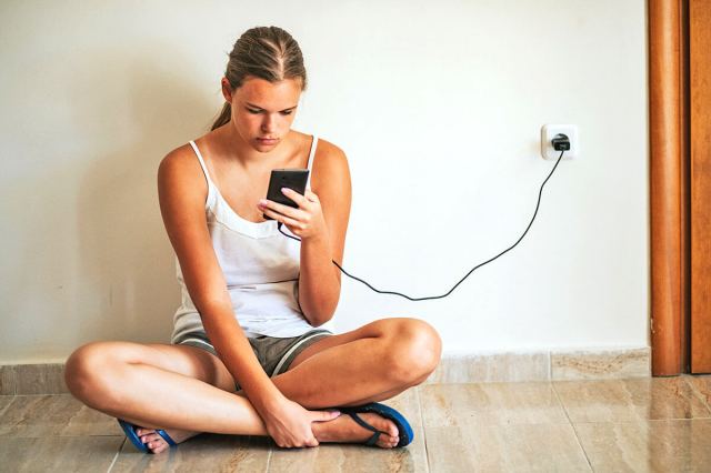 Woman sitting cross-legged looking at her phone, which is plugged into the wall