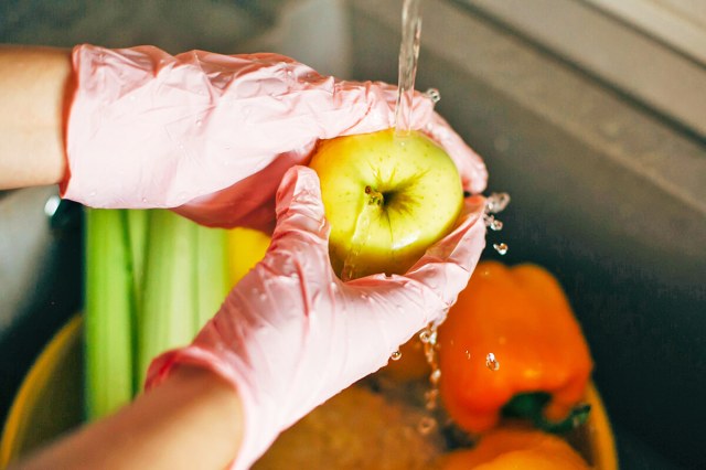 Person wearing gloves and washing an apple under running water