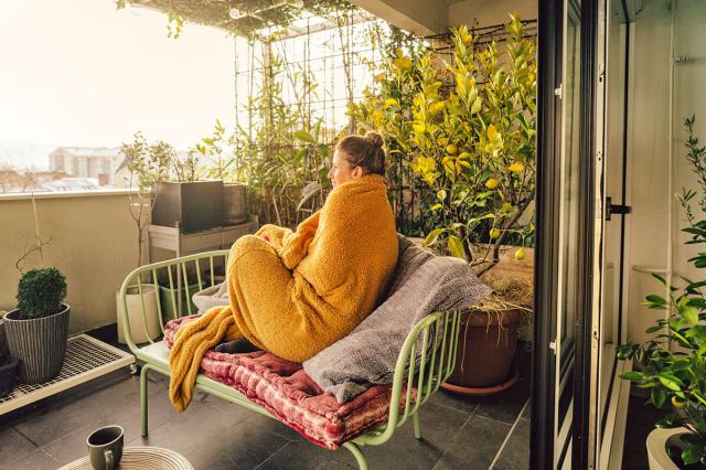 Woman wrapped in a yellow blanket sitting on a couch on her balcony