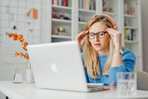 Woman sitting in front of laptop with her hands on her temples