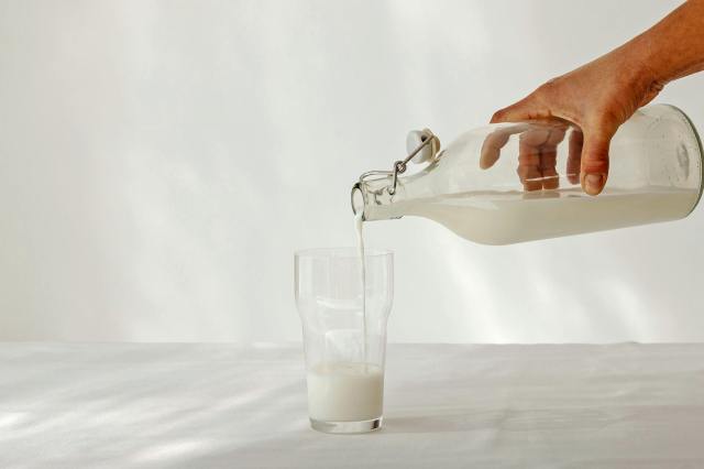 Person pouring milk from a clear jg into a glass