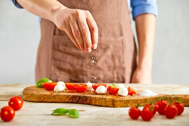 Person in an apron sprinkling salt on tomatoes and mozzarella